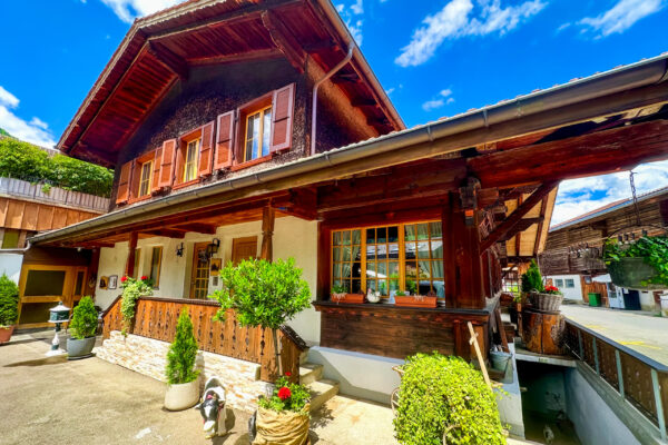 Chalet Simmi-34 Das Chalet Simmi von außen: ein wunderschönes Chalet im alpinen Flair, grüne Bäume vor einem blauen Himmel mit Bergen im Hintergrund