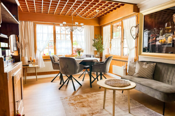 Chalet Simmi-38 Chalet Simmi: Sitzbereich in der Stube, wirkt sehr einladend mit warmen Licht. Ein Kronleuchter kommt aus der Holzdecke und darunter steht ein gedeckter Tisch mit Blumenstrauß und vier Stühlen drum herum, sehr edel eingerichtet