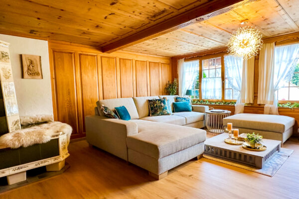 Chalet Simmi-6 Das Wohnzimmer im Chalet Simmi mit riesengroßer Couch, einem Tisch, warmen Licht und daneben ein kuscheliger Kachelofen